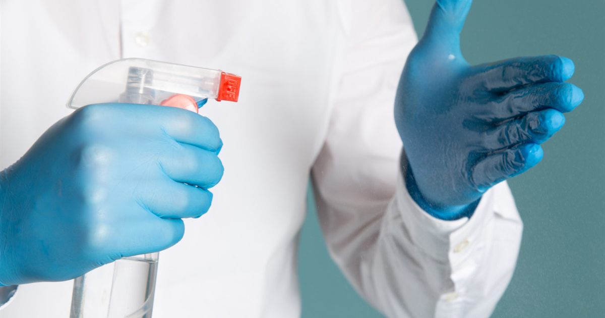Blue-gloved hands holding a spray bottle and cleaning cloth